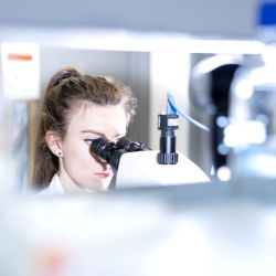 Woman looks into lens of microscope in foreground