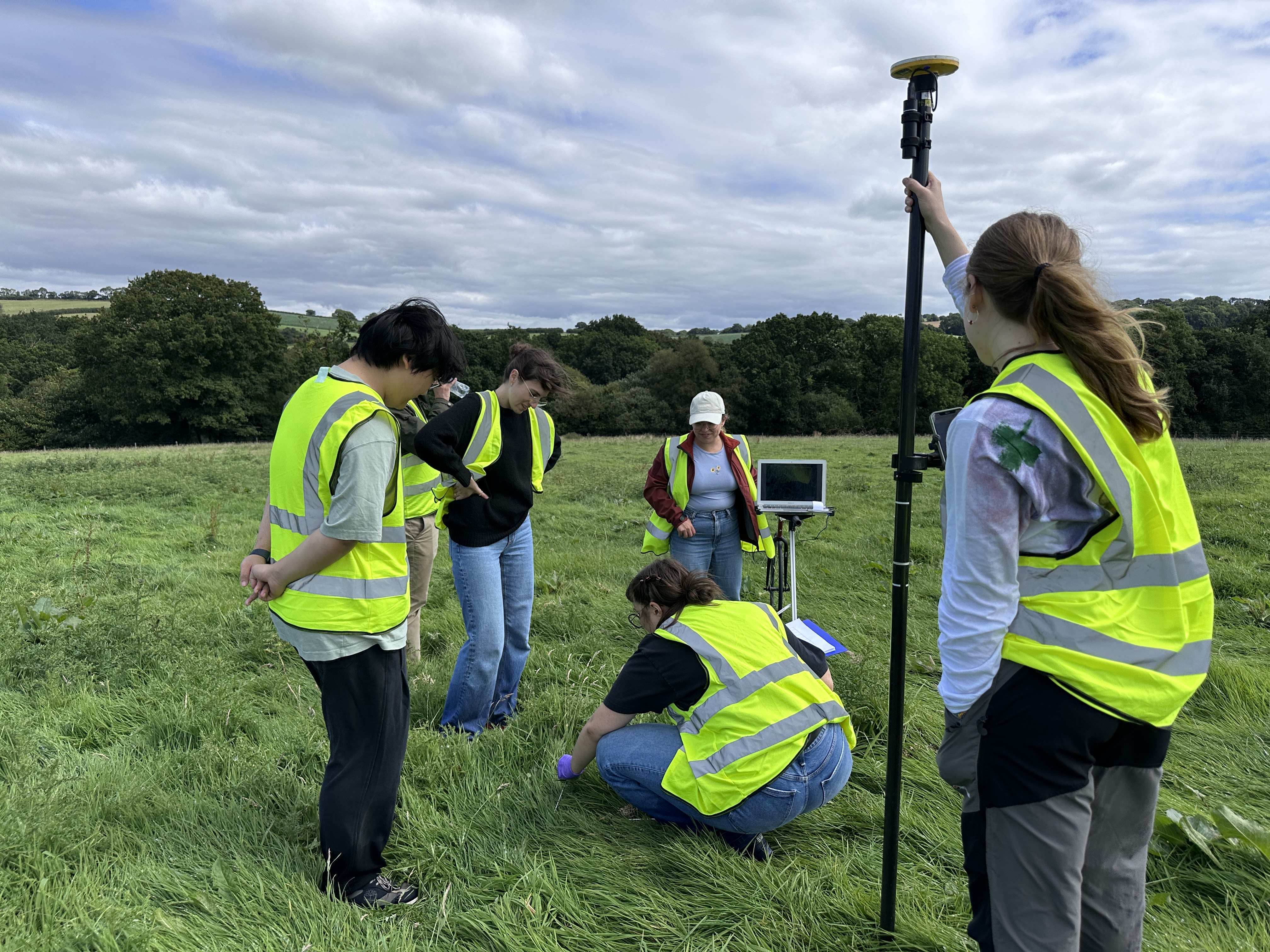 Five people in high-vis in a grassy field looking at a point in the ground