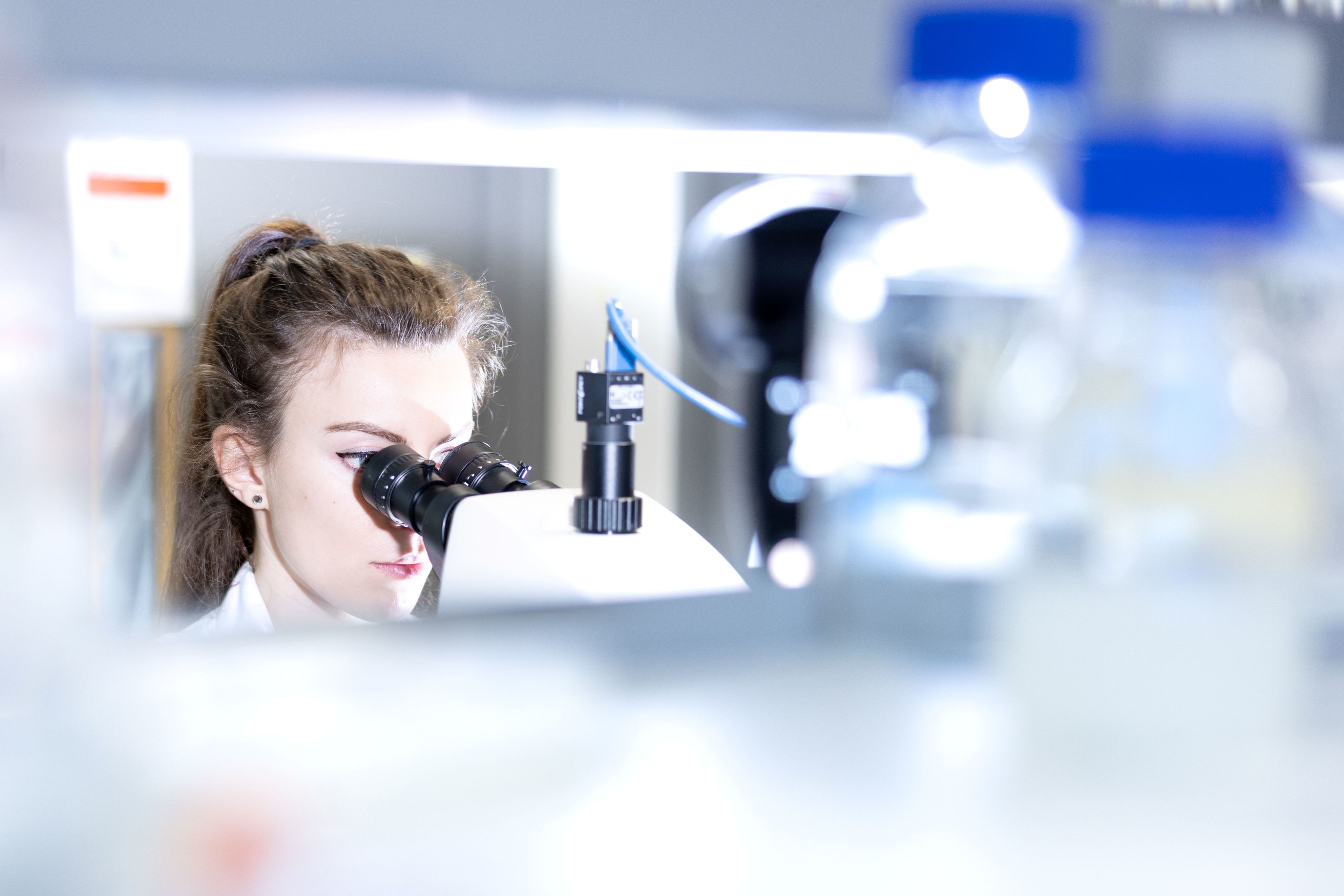 Woman looks into lens of microscope in foreground.