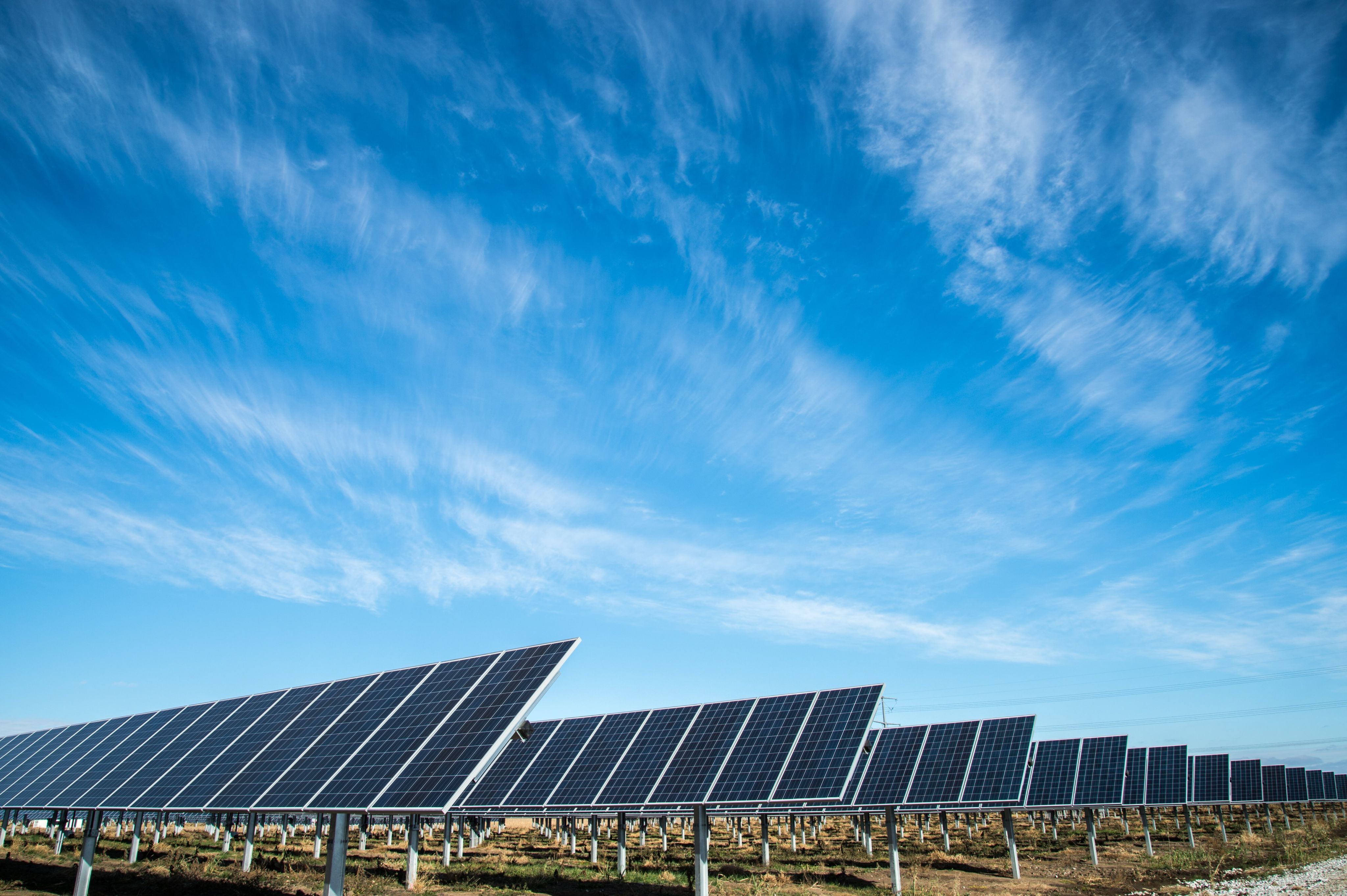 Solar panels under blue sky with light clouds.
