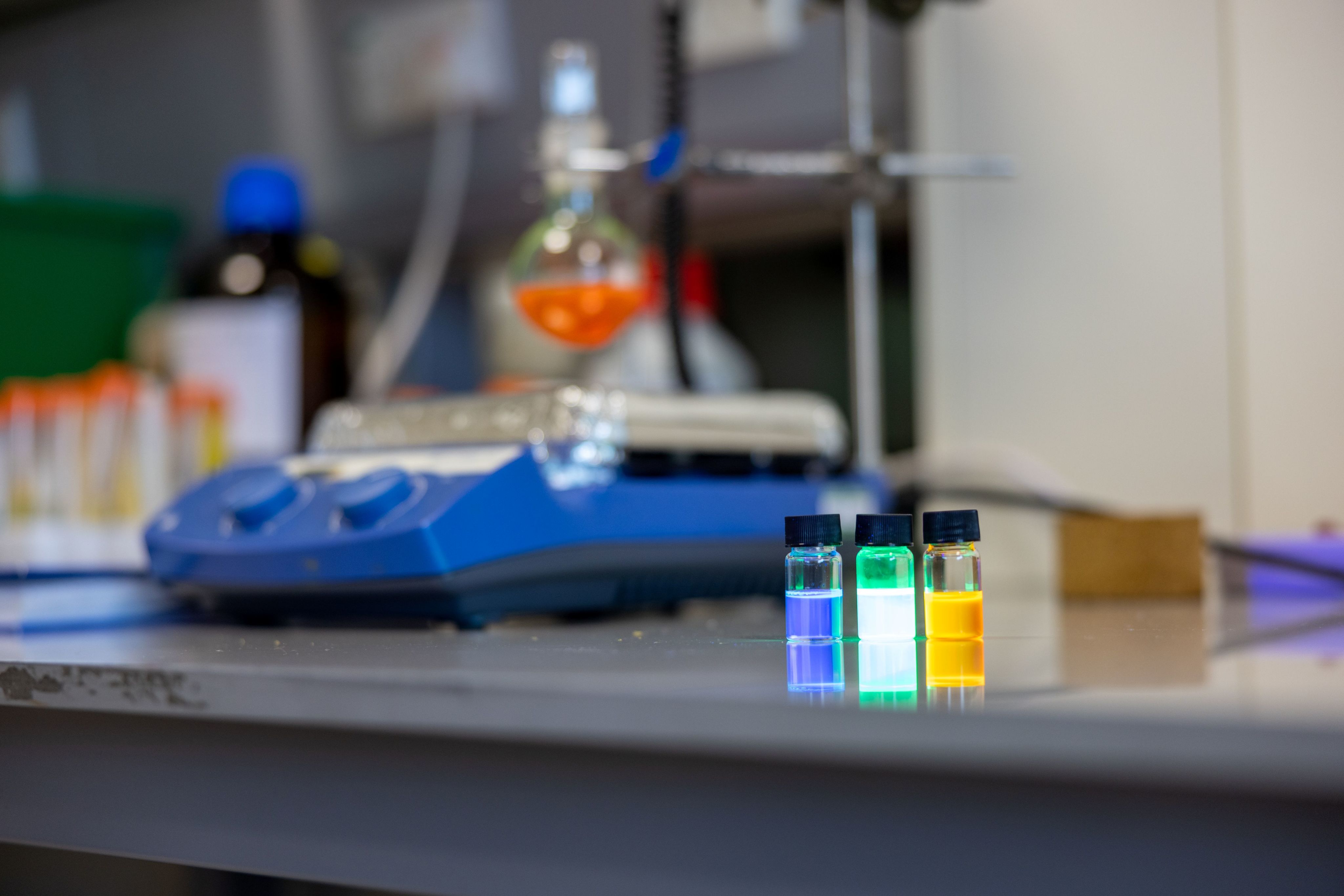 Shot of 3 small test tubes with lids, that are slightly lit up. Blue, white and yellow.