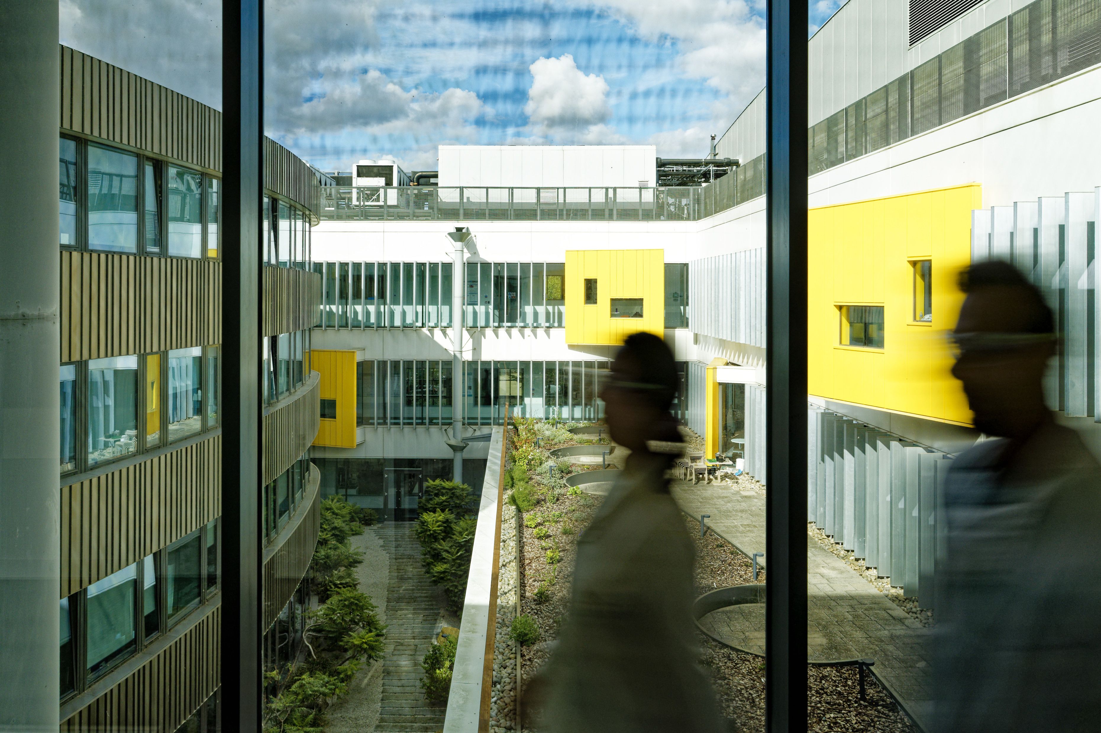 Two people blurred as they walk across corridor with inner courtyard of CEB in background.