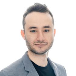 A man in a grey jacket looks towards the camera