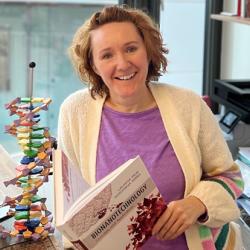 Ljiljana Fruk in her office holding the Bionanotechnology textbook and standing next to a model of DNA
