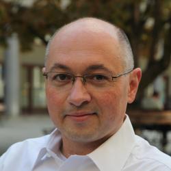 Bald, white man with glasses in white shirt smiling gently at the camera