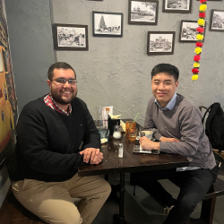 Ziad and Zheng Jie smile at the camera in a cafe/bar setting with drinks on the table. Dressed in smart casual clothes.