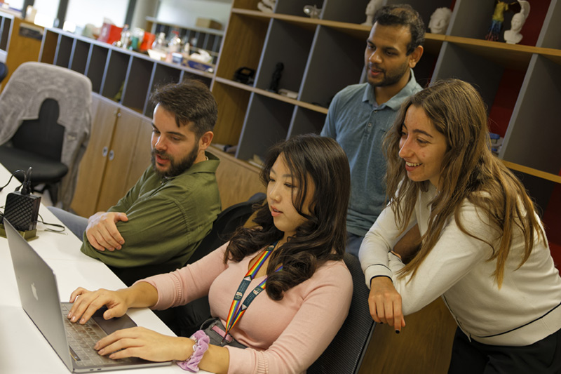 Four students smile as they crowd round one computer.