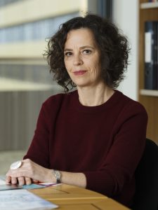 A woman sits at a table looking towards the camera