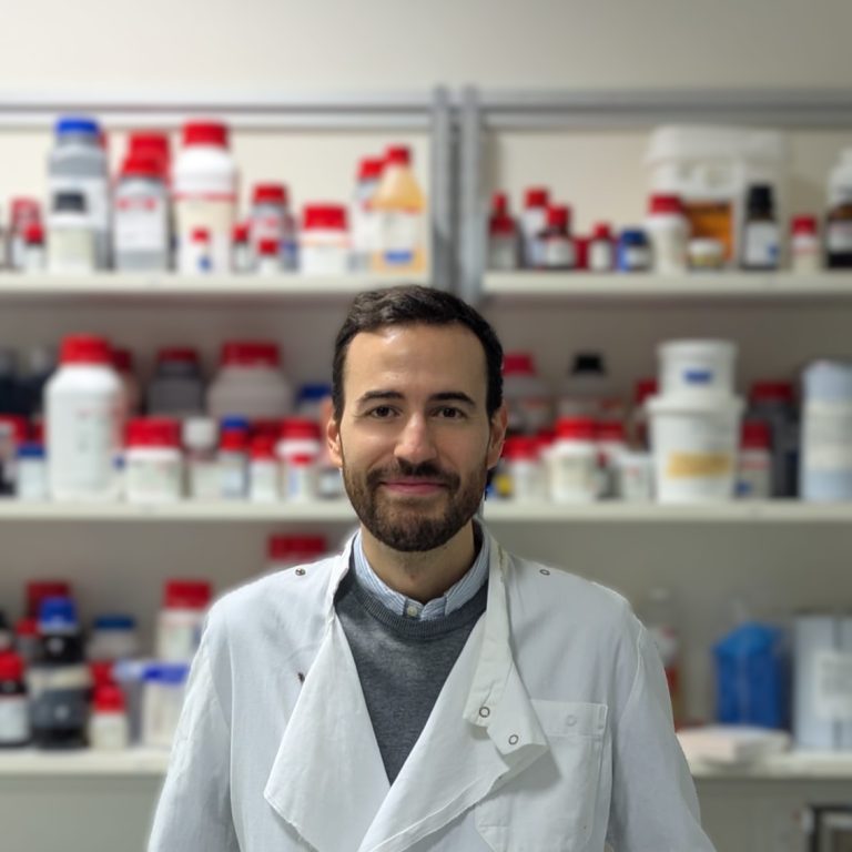 Portrait of a man in a lab coat. A lab forms the background.