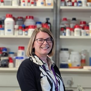 Portrait of a woman with glasses. A lab environment in the background.