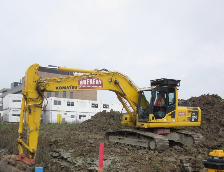 A yellow excavator works to dig out a construction site.