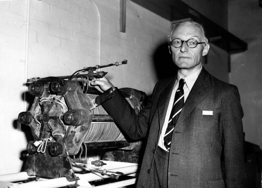 A black and white photo of a man standing next to a piece of scientific equipment.