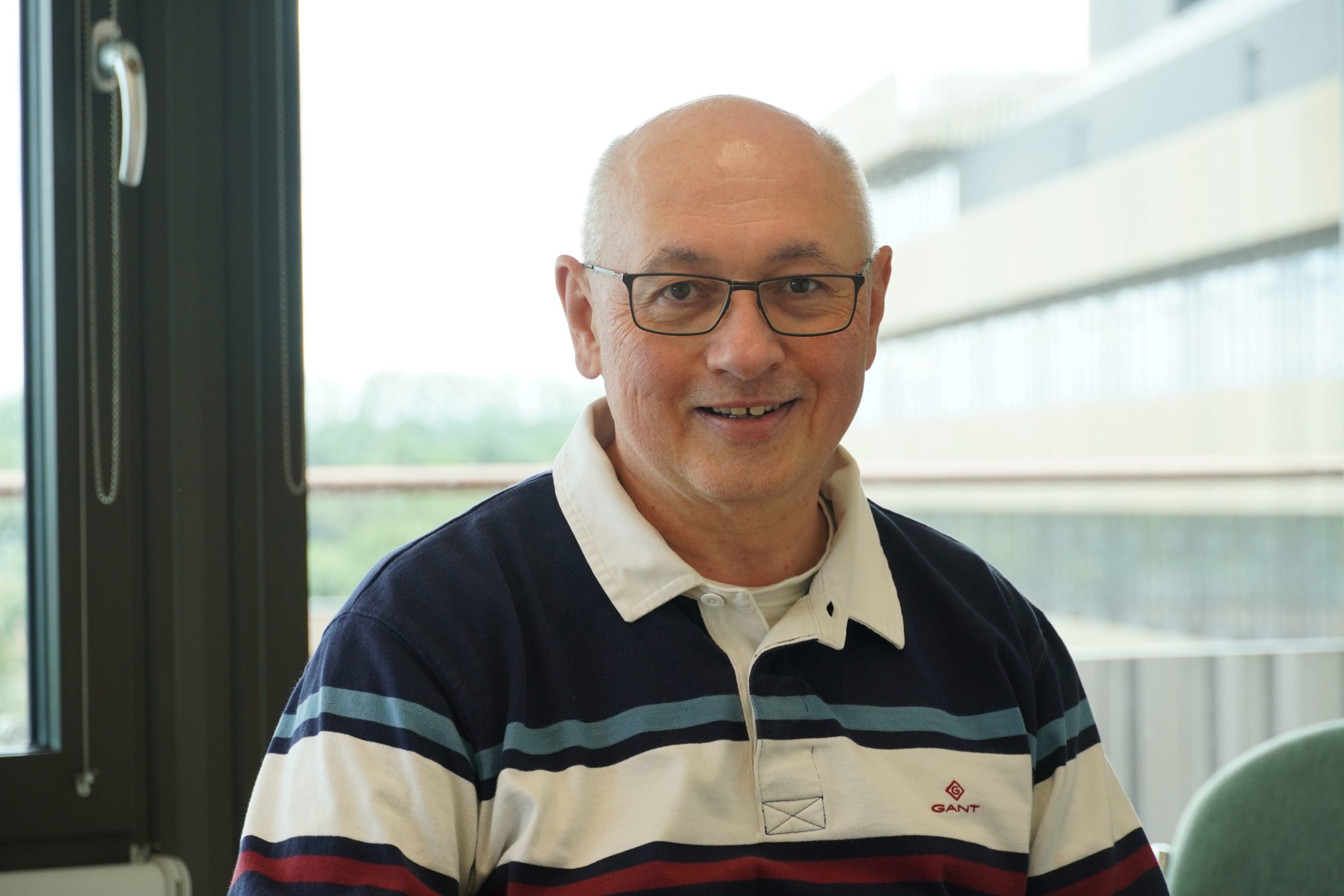 Markus Kraft headshot in CEB office with MSM in the background. In blue striped polo shirt.