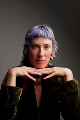 Professional headshot of Jennifer Crouch, dressed in black with dark backdrop. Hands held up as a table with chin resting on back of hands.