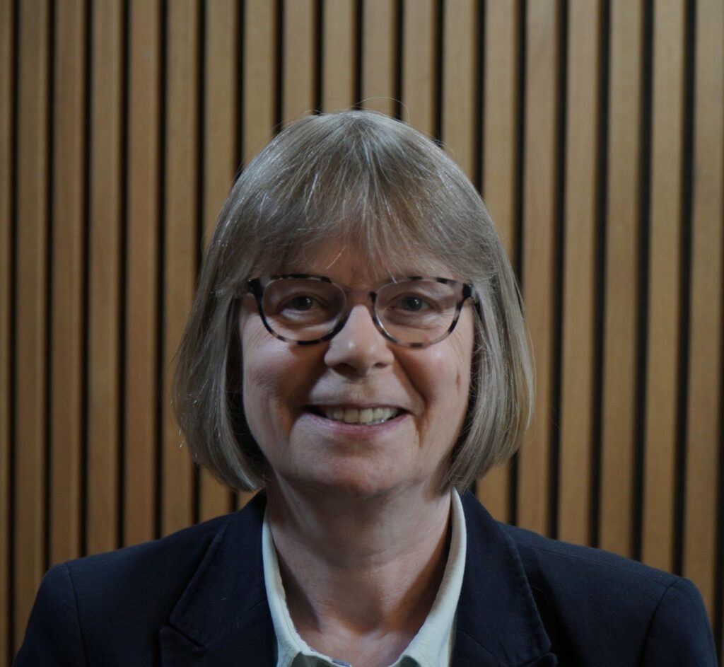 A woman in spectacles smiles at the camera.